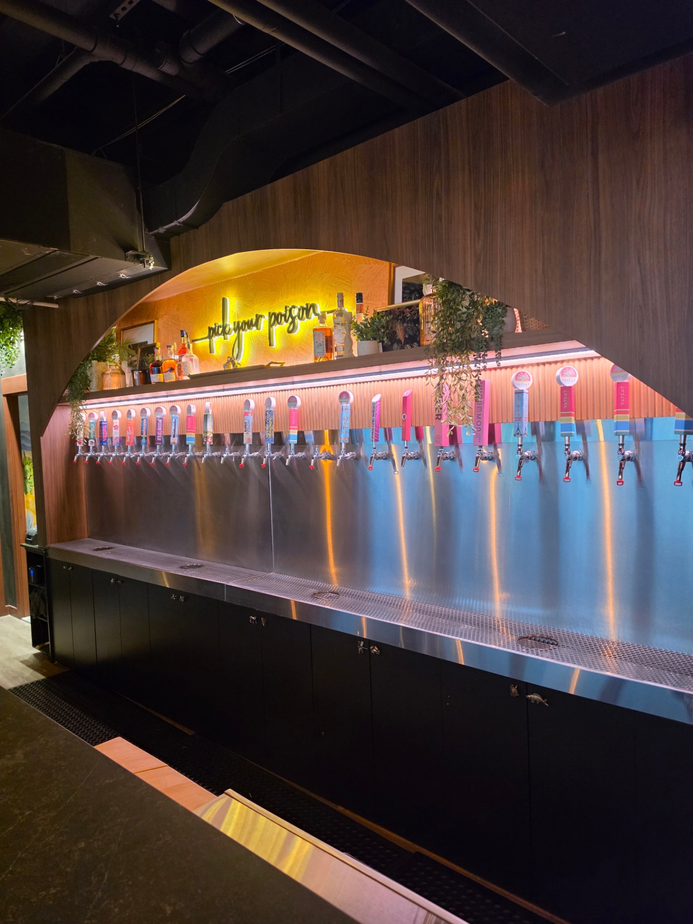 Upstairs tap wall under the signature arch with 'pick your poison' neon
